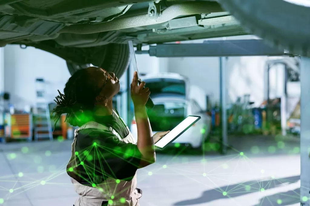 woman inspecting the underside of a car with a light holding a tablet with green plexus overlayed