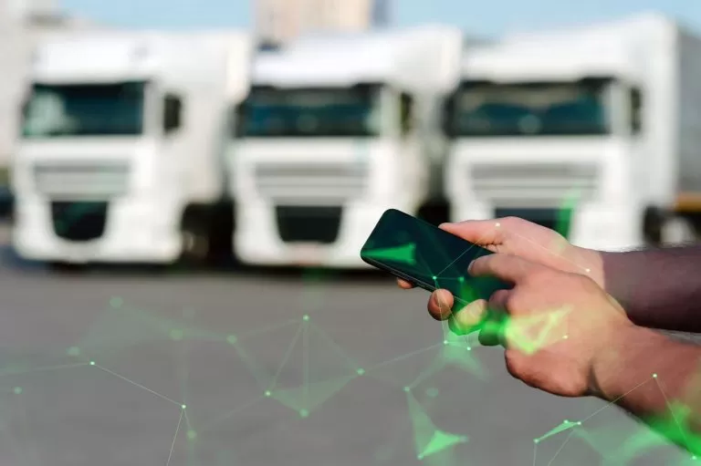 Lorry fleet in background with hands holding phone in foreground