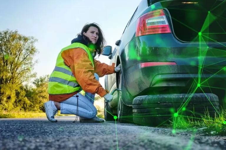 woman in hi-vis changing car tyre on the side of road with green plexus overlayed