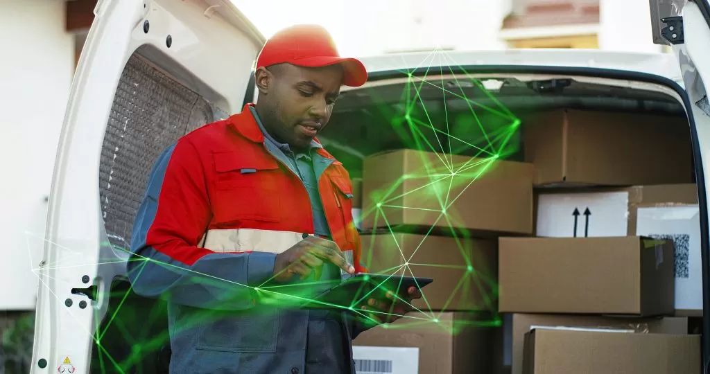 young delivery man red costume using tabekt whilst delivering parcels outdoors green plexus